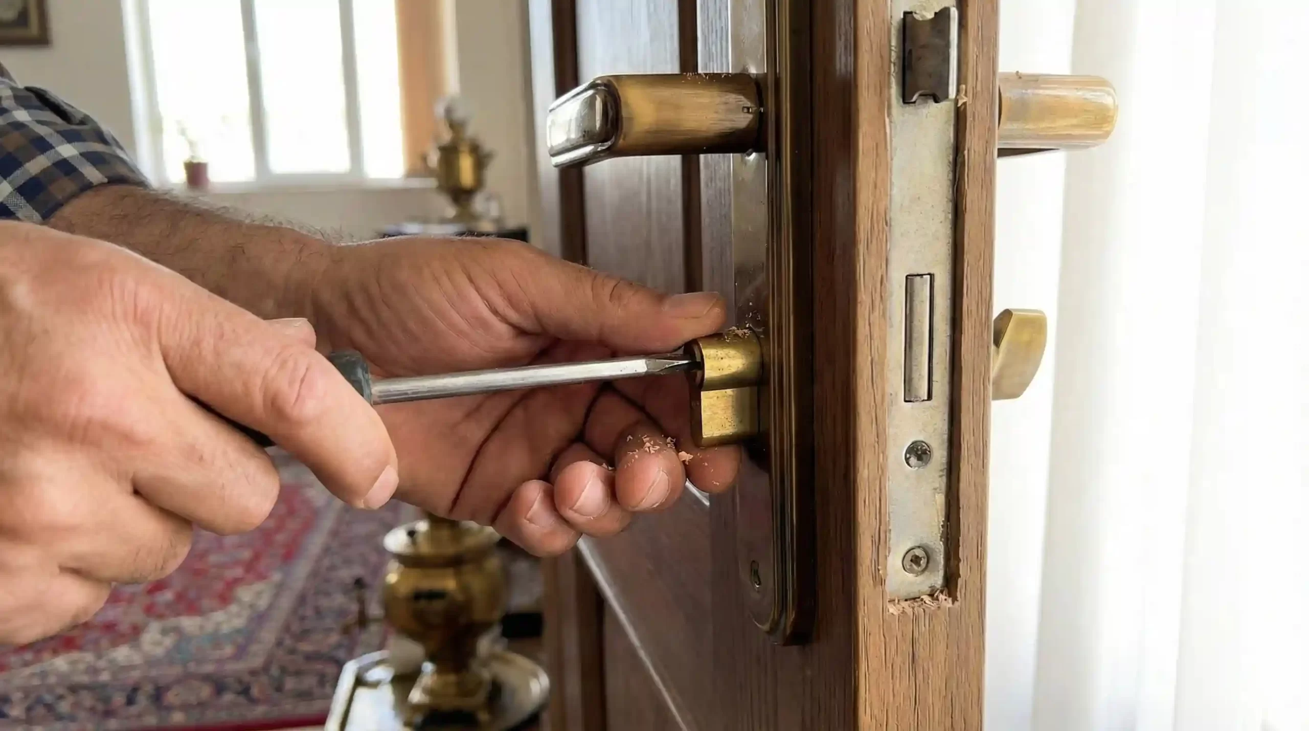 نمای نزدیک از تعویض مغزی قفل درب چوبی توسط تعمیرکار حرفه‌ای.